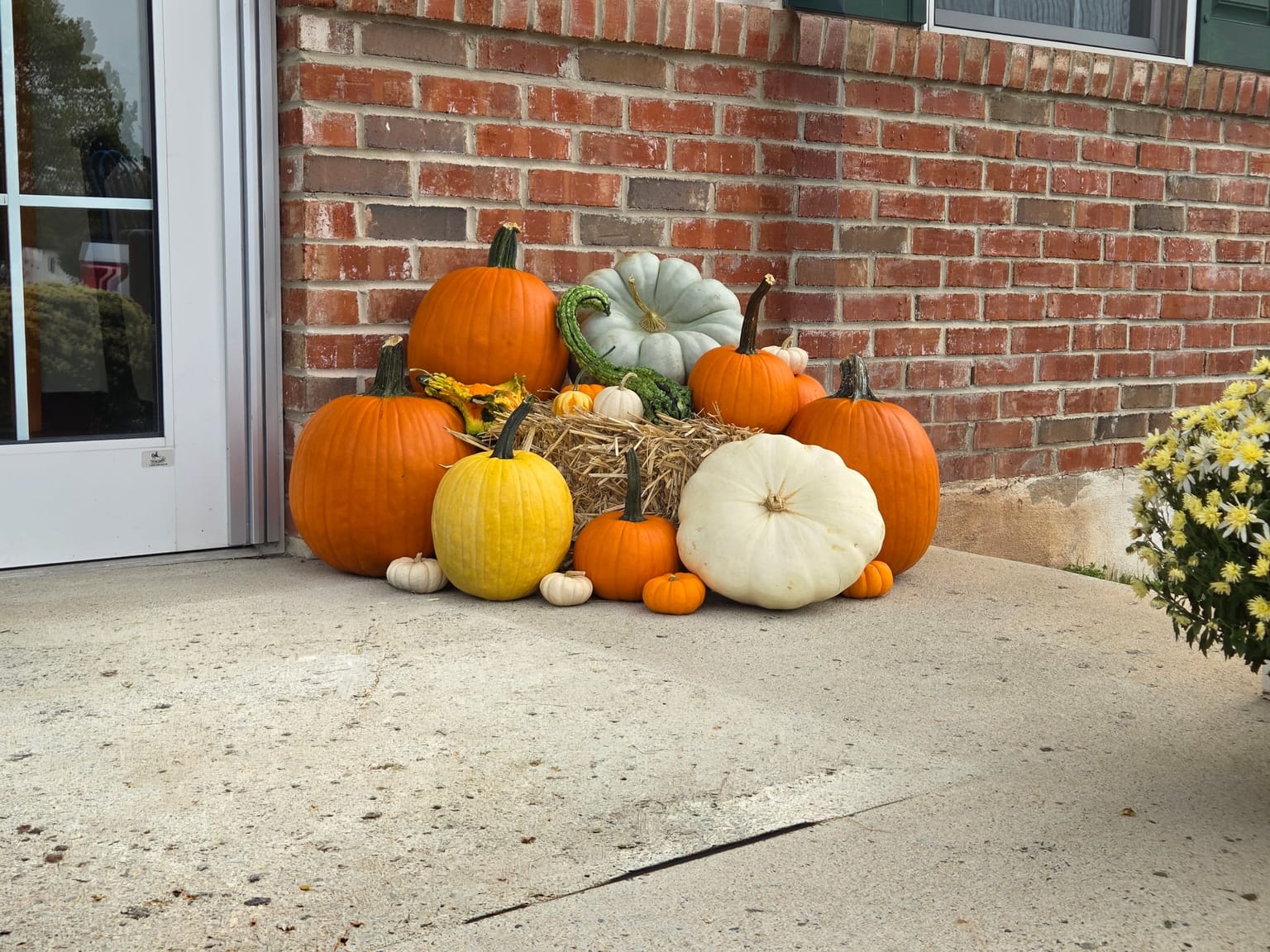 Pumpkins, gourds and a straw bale grouped against a brick wall beside a glass entrance door
