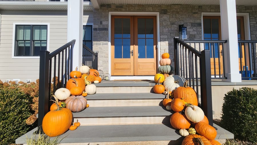 Pumpkins massed down both sides of wide steps leading to wood-and-glass double doors, between black railings