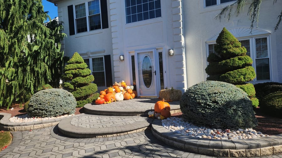 A wide view of a large stucco home, with a pumpkin display and hay bale set at the front entrance between clipped topiaries