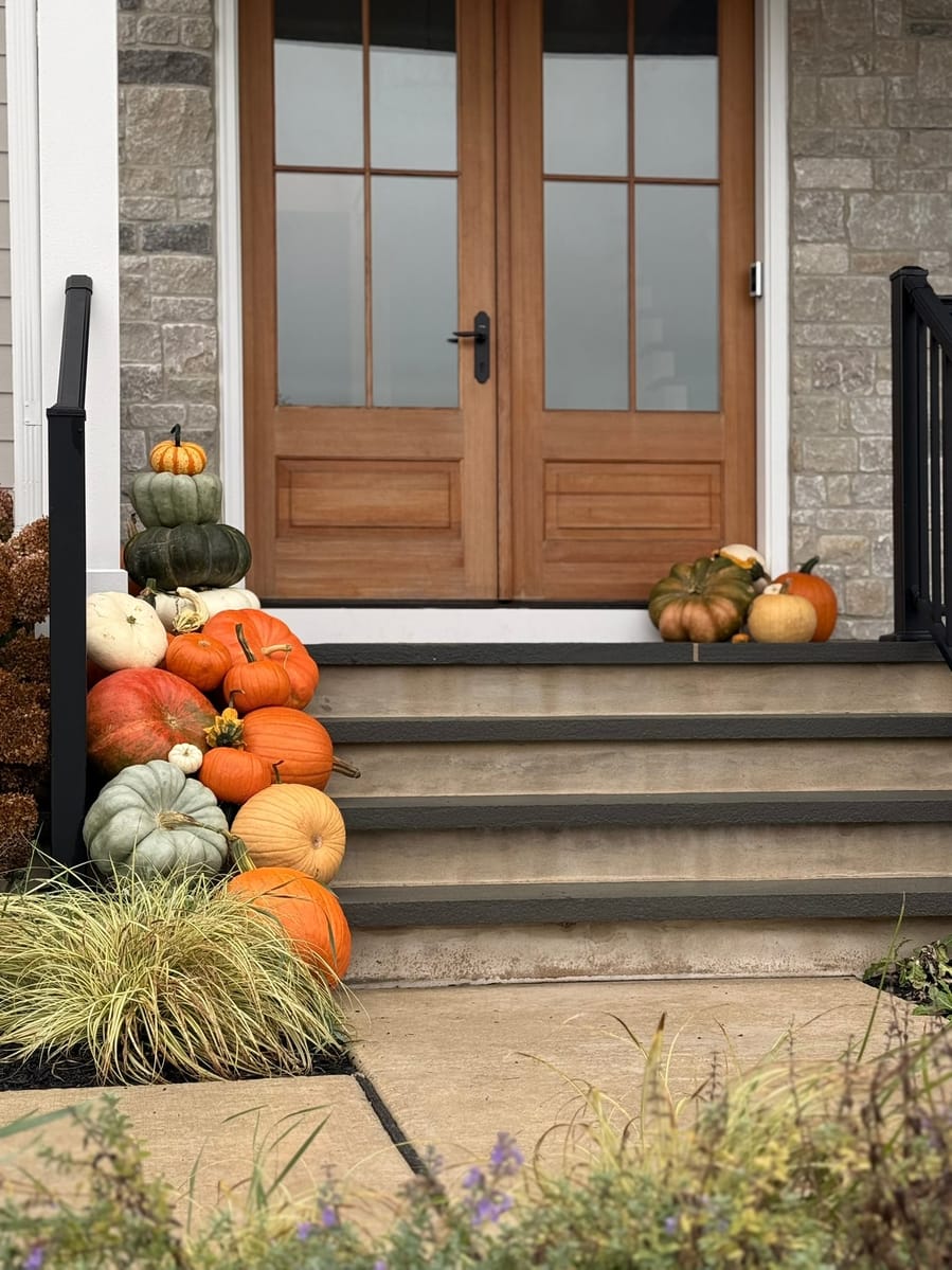Pumpkins and gourds stacked down one side of the steps to a pair of wood-and-glass front doors