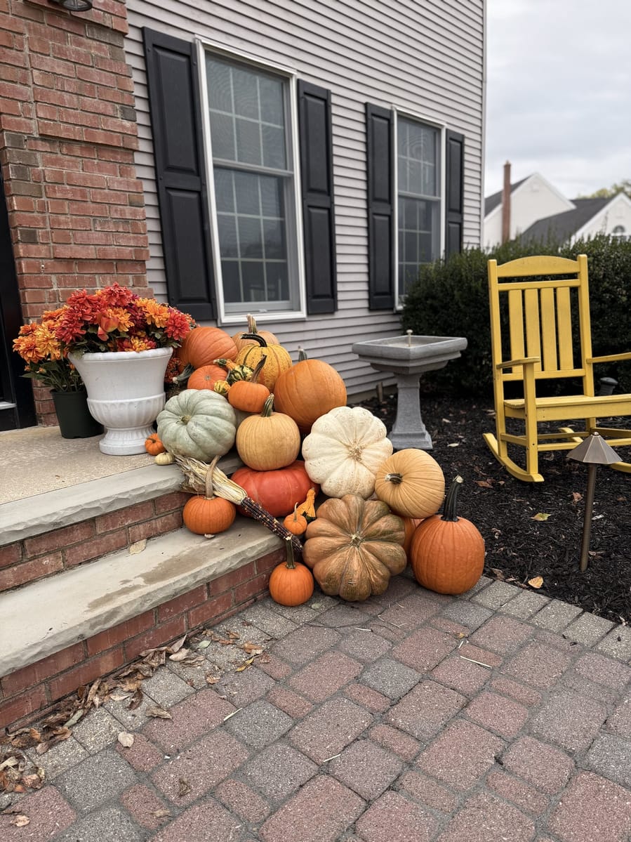 Pumpkins and gourds spilling from a brick step onto the walkway, with a yellow rocking chair and birdbath alongside