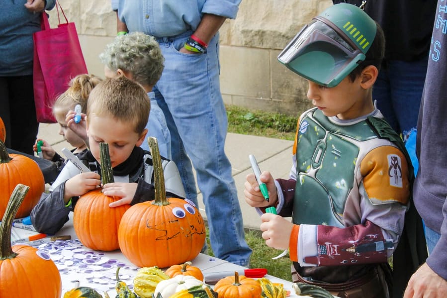 Children in costume decorating pumpkins with markers and googly eyes at an outdoor table