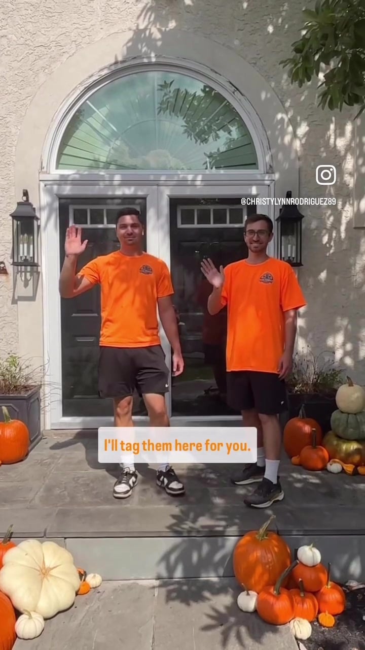 Two Penn Pumpkin Co crew members in orange shirts waving in front of a finished porch display