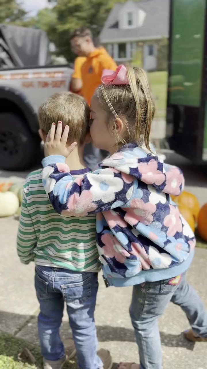 Two young children standing together beside the delivery truck as pumpkins are unloaded